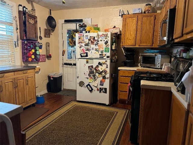 5621 Tchoupitoulas St, New Orleans, LA 70115 - kitchen with stainless steel microwave, freestanding refrigerator, black range with gas stovetop, dark wood-type flooring, and brown cabinetry