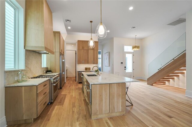 7104 Coliseum St, New Orleans, LA 70118 - kitchen with high end appliances, a sink, custom exhaust hood, light wood-style flooring, and a kitchen island with sink