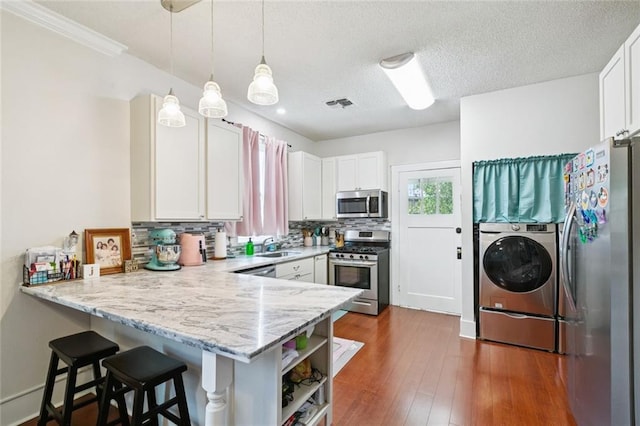 220 Moss Ln, River Ridge, LA 70123 - kitchen featuring appliances with stainless steel finishes, washer / dryer, a peninsula, decorative backsplash, and white cabinets