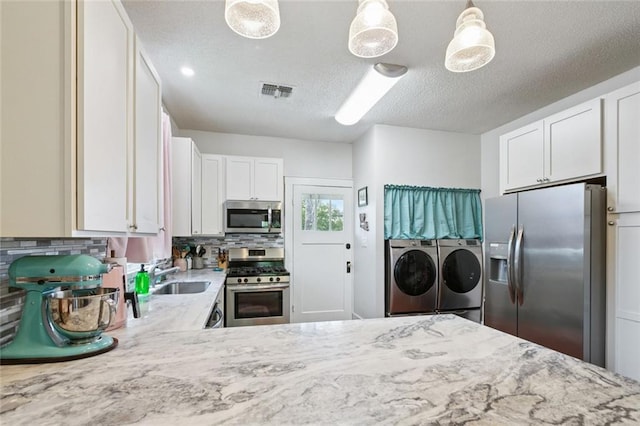 220 Moss Ln, River Ridge, LA 70123 - kitchen with washing machine and dryer, appliances with stainless steel finishes, a sink, light stone counters, and decorative backsplash