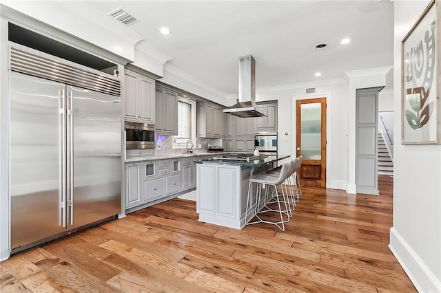 3 Fairview Ct, Metairie, LA 70005 - kitchen featuring built in appliances, island range hood, gray cabinetry, ornamental molding, and a kitchen breakfast bar
