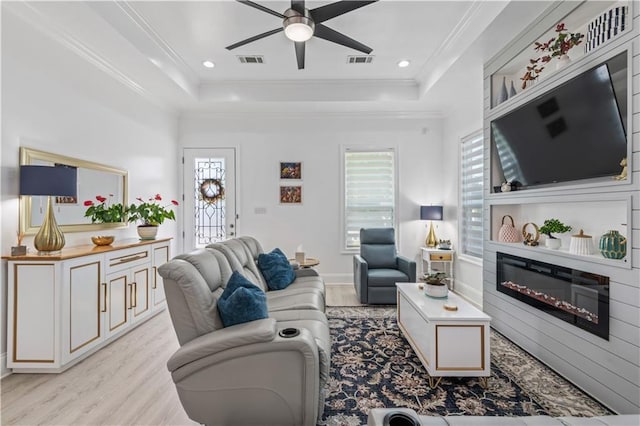 2828 Mistletoe St, New Orleans, LA 70118 - living area featuring light wood-style floors, a ceiling fan, a glass covered fireplace, a tray ceiling, and crown molding