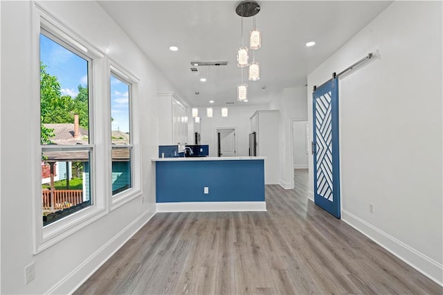 3414 Monroe St, New Orleans, LA 70118 - kitchen with a barn door, light wood finished floors, white cabinets, light countertops, and a peninsula