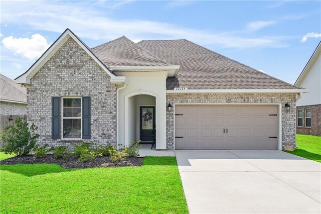 22039 Giselle Dr, Mandeville, LA 70471 - french country inspired facade featuring driveway, an attached garage, a front lawn, brick siding, and roof with shingles