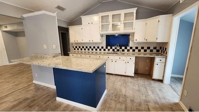 146 Elodie Ave, Harahan, LA 70123 - kitchen with light wood-style floors, white cabinetry, lofted ceiling, a peninsula, and tasteful backsplash