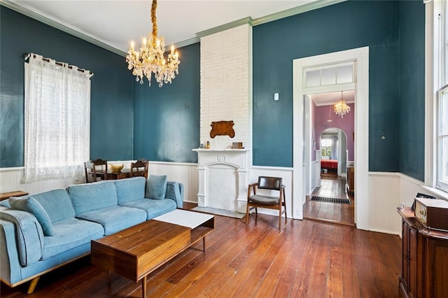 717 Nunez St, New Orleans, LA 70114 - living room featuring arched walkways, a chandelier, wood-type flooring, a wainscoted wall, and ornamental molding