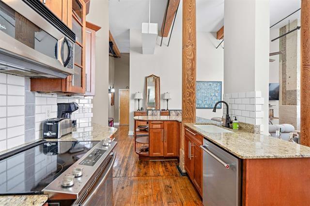 920 Poeyfarre St Unit 176, New Orleans, LA 70130 - kitchen with appliances with stainless steel finishes, brown cabinetry, light stone countertops, dark wood-style flooring, and a towering ceiling