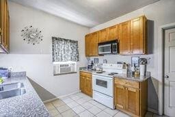 291618 Andover St, Jefferson, LA 70121 - kitchen with stainless steel microwave, white electric range oven, brown cabinets, light tile patterned floors, and light countertops