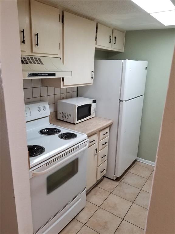 6220 Riverside Dr Unit 556, Metairie, LA 70003 - kitchen with white appliances, under cabinet range hood, decorative backsplash, light countertops, and light tile patterned flooring