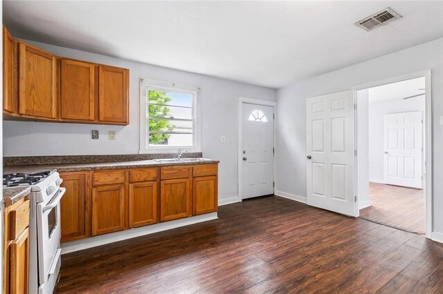 220002 Delille St, Chalmette, LA 70043 - kitchen featuring white gas range oven, brown cabinets, dark wood-style floors, dark countertops, and a sink