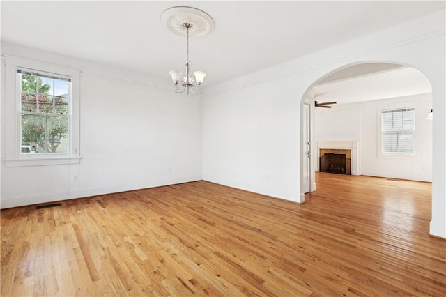 5524 S Galvez St, New Orleans, LA 70125 - empty room featuring arched walkways, light wood-style flooring, a tile fireplace, and a chandelier