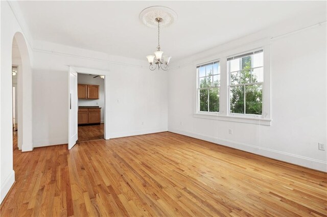 5524 S Galvez St, New Orleans, LA 70125 - empty room with a chandelier, light wood finished floors, arched walkways, and baseboards