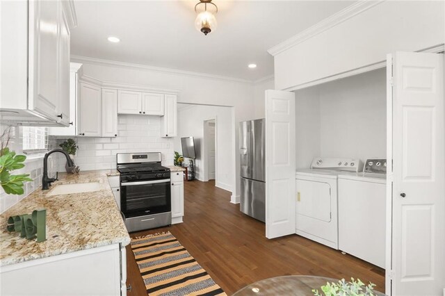 5124 Painters St, New Orleans, LA 70122 - kitchen with appliances with stainless steel finishes, washer and clothes dryer, ornamental molding, white cabinets, and tasteful backsplash