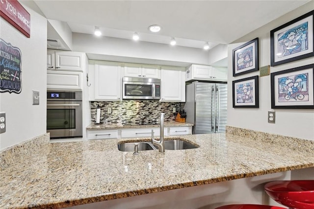 585 Beau Chene Dr, Mandeville, LA 70471 - kitchen with stainless steel appliances, a sink, light stone counters, white cabinetry, and a breakfast bar