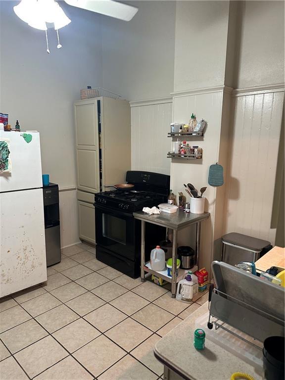 70911 Evelina St, New Orleans, LA 70114 - kitchen with gas stove, freestanding refrigerator, ceiling fan, light tile patterned floors, and wainscoting