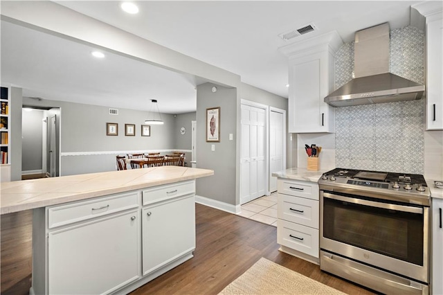 1924 Cammie Ave, Metairie, LA 70003 - kitchen featuring stainless steel gas range, wall chimney exhaust hood, light countertops, white cabinets, and tasteful backsplash