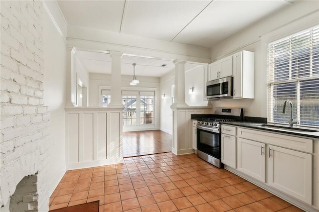 3019 Burdette St, New Orleans, LA 70125 - kitchen featuring stainless steel appliances, a sink, decorative columns, light tile patterned floors, and dark countertops