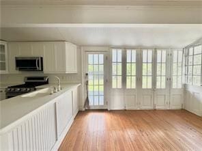 110 Mulberry Ave, Mandeville, LA 70448 - kitchen featuring stainless steel microwave, gas range oven, light wood-type flooring, light countertops, and white cabinetry