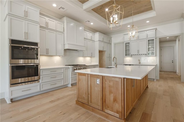 391 Rue Charlotte St, Madisonville, LA 70447 - kitchen with appliances with stainless steel finishes, a tray ceiling, a chandelier, light wood-type flooring, and crown molding