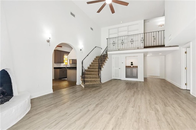 5117 Academy Dr, Metairie, LA 70003 - unfurnished living room featuring ceiling fan, a towering ceiling, stairs, light wood finished floors, and arched walkways