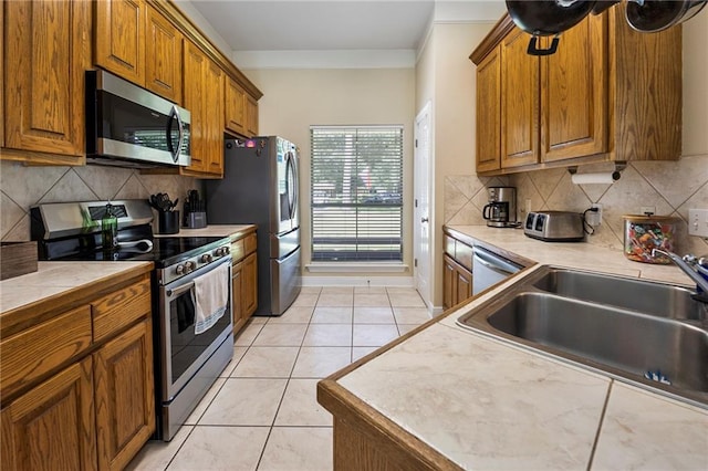 72158 Mill Rd, Abita Springs, LA 70420 - kitchen featuring appliances with stainless steel finishes, a sink, brown cabinetry, decorative backsplash, and crown molding