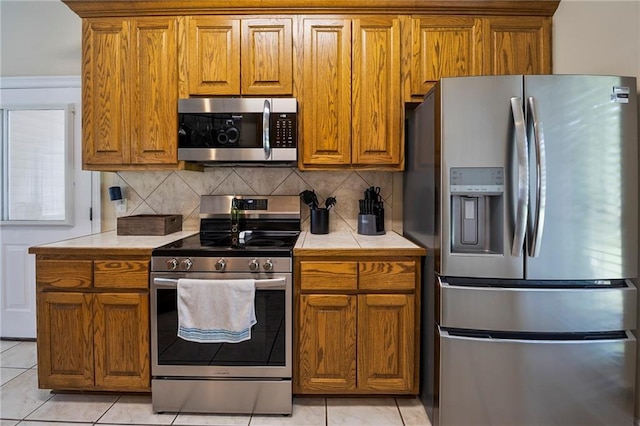 72158 Mill Rd, Abita Springs, LA 70420 - kitchen featuring stainless steel appliances, tile countertops, brown cabinetry, tasteful backsplash, and light tile patterned floors