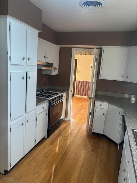 3107 Metairie Heights Ave, Metairie, LA 70002 - kitchen with black gas stove, light wood finished floors, under cabinet range hood, and white cabinetry