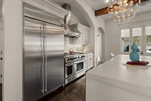 1322 S Jahncke Ave, Covington, LA 70434 - kitchen featuring premium appliances, arched walkways, beamed ceiling, tasteful backsplash, and white cabinetry
