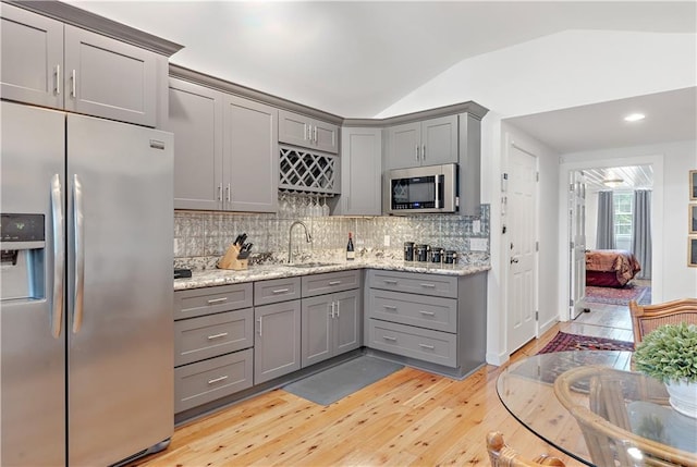 20263 Brunning Rd, Covington, LA 70435 - kitchen featuring appliances with stainless steel finishes, gray cabinetry, a sink, vaulted ceiling, and light wood-type flooring