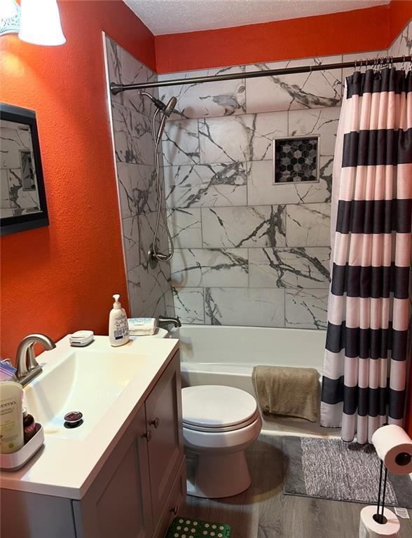 4405 Cartier Ave, New Orleans, LA 70122 - full bath with a textured wall, shower / tub combo with curtain, vanity, toilet, and wood finished floors