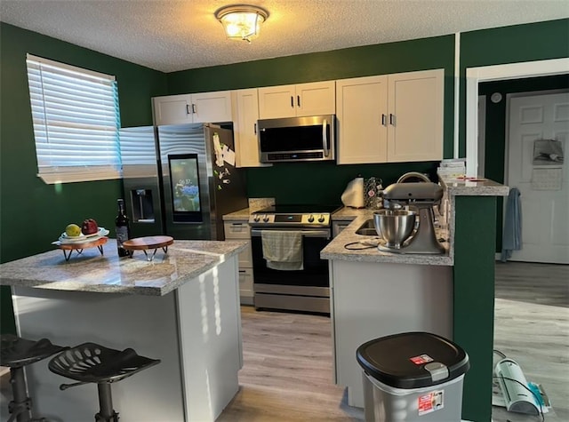 4405 Cartier Ave, New Orleans, LA 70122 - kitchen featuring stainless steel appliances, light wood-type flooring, white cabinets, a textured ceiling, and a kitchen breakfast bar