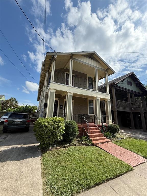 4218 S Liberty St, New Orleans, LA 70115 - view of front facade with a balcony, covered porch, driveway, and a front lawn