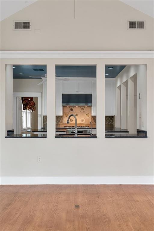 324 Fairway Dr, New Orleans, LA 70124 - detailed view of under cabinet range hood, wood finished floors, tasteful backsplash, and white cabinetry