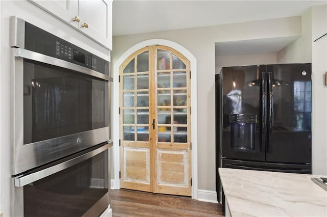 2351 Ormond Blvd, Destrehan, LA 70047 - kitchen with black fridge with ice dispenser, stainless steel double oven, dark wood-style flooring, baseboards, and light stone counters