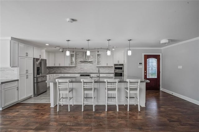 9509 Robin Ln, River Ridge, LA 70123 - kitchen with wall chimney exhaust hood, appliances with stainless steel finishes, decorative backsplash, a kitchen bar, and a kitchen island with sink