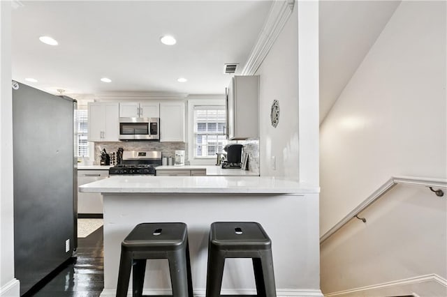 1030 Kerlerec St Unit 4, New Orleans, LA 70116 - kitchen featuring stainless steel microwave, gas range oven, a kitchen breakfast bar, backsplash, and a peninsula