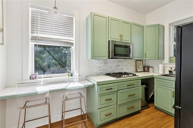 6945 Milne Blvd, New Orleans, LA 70124 - kitchen featuring green cabinets, stainless steel appliances, decorative backsplash, light countertops, and light wood-type flooring