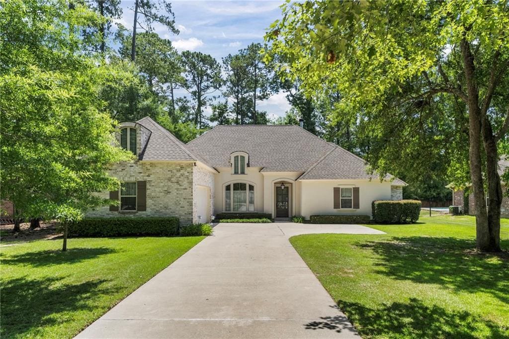 1765 Old Mandeville Ln, Mandeville, LA 70448 - french provincial home with concrete driveway, a front yard, stucco siding, and an attached garage