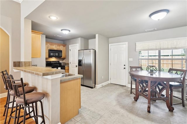 70323 11th St, Covington, LA 70433 - kitchen with black appliances, a kitchen bar, baseboards, arched walkways, and light brown cabinetry