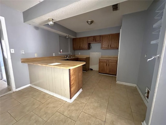 2216 Teal St, Slidell, LA 70460 - kitchen with a peninsula, brown cabinetry, baseboards, light countertops, and light tile patterned floors