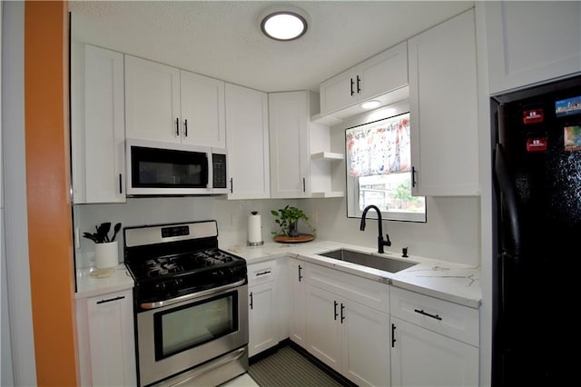 213 Travis Dr, Westwego, LA 70094 - kitchen with white microwave, stainless steel gas range, freestanding refrigerator, a sink, and white cabinetry
