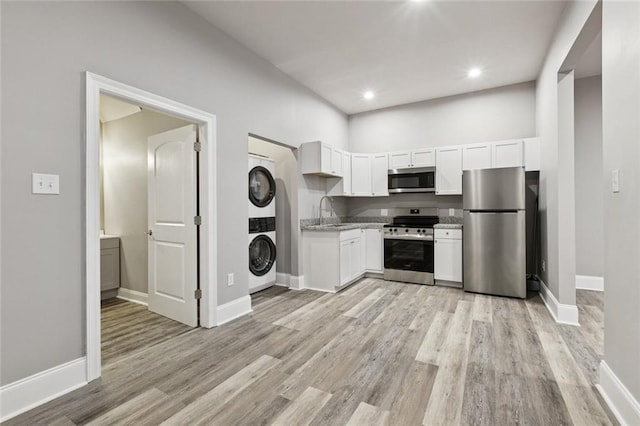 1400 Woodland Hwy, Belle Chasse, LA 70037 - kitchen featuring stainless steel appliances, stacked washing machine and dryer, a sink, light wood finished floors, and white cabinets
