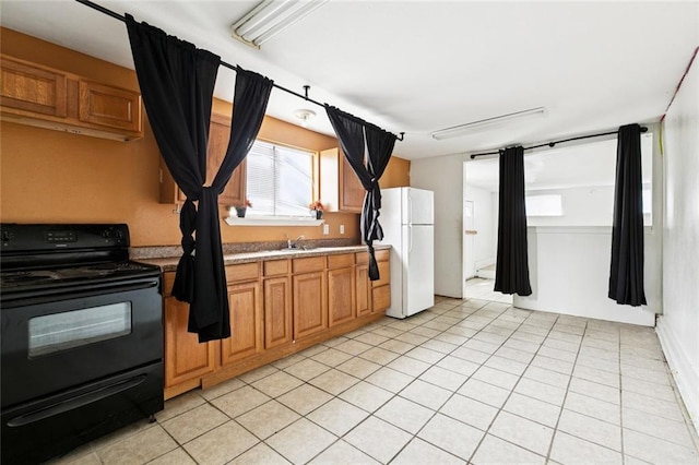 3500 Clematis St, New Orleans, LA 70123 - kitchen featuring black electric range oven, freestanding refrigerator, light tile patterned flooring, light countertops, and brown cabinetry