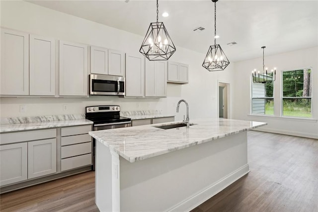 69206 4th Ave, Covington, LA 70433 - kitchen with appliances with stainless steel finishes, wood finished floors, a chandelier, a kitchen island with sink, and light stone countertops