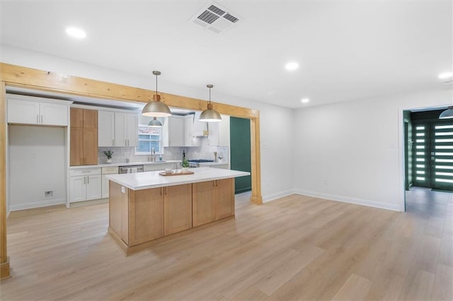 145 Macque Dr, Harahan, LA 70123 - kitchen featuring wall chimney range hood, light wood-type flooring, light countertops, white cabinets, and backsplash