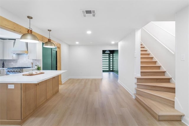 145 Macque Dr, Harahan, LA 70123 - kitchen with wall chimney exhaust hood, light wood-style flooring, white cabinetry, stove, and a center island