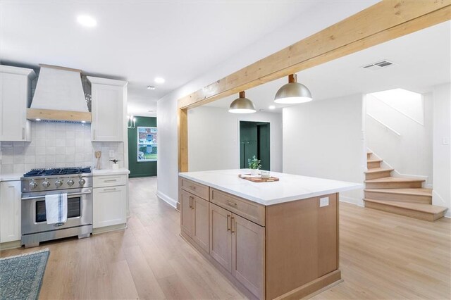 145 Macque Dr, Harahan, LA 70123 - kitchen featuring appliances with stainless steel finishes, custom exhaust hood, light wood-type flooring, tasteful backsplash, and a kitchen island