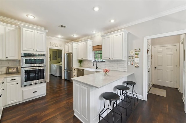 103 Century Oaks Ln, Mandeville, LA 70471 - kitchen featuring appliances with stainless steel finishes, independent washer and dryer, a kitchen bar, white cabinetry, and a peninsula