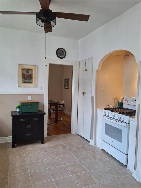 4712 Lafaye St, New Orleans, LA 70122 - kitchen with gas range gas stove, a ceiling fan, arched walkways, light tile patterned floors, and white cabinets