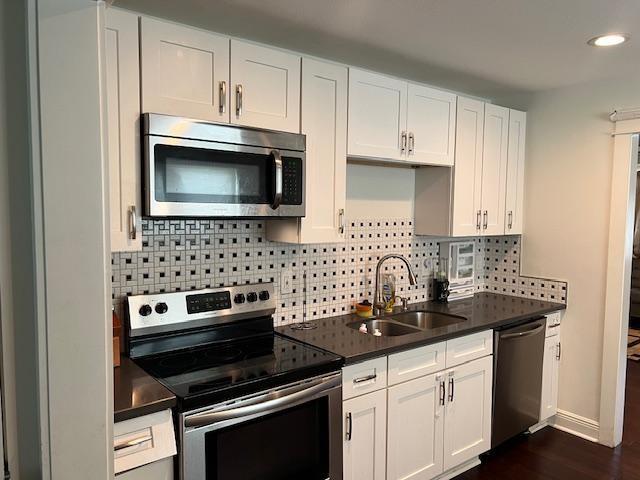 7109 Dreux Ave, New Orleans, LA 70126 - kitchen featuring stainless steel appliances, decorative backsplash, dark countertops, white cabinetry, and recessed lighting